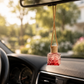 Car air freshener hanging from a car's rearview mirror with a blurred outdoor background