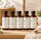 Five bottles of Roses Natural laundry detergent on a wooden surface with a basket and towels in the background.