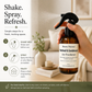 Hand holding a bottle of Roses Natural air freshener with usage instructions in a living room setting.