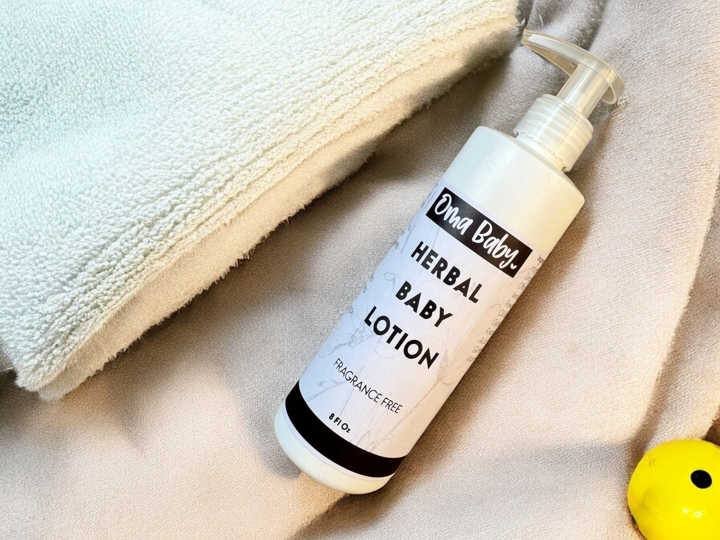 Oma Baby herbal baby lotion bottle on a textured surface with a towel and yellow object.