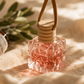 Roses Natural Clear glass air freshener with wooden top on a textured surface with blurred background